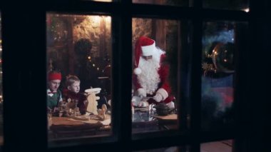 Santa Claus residence outside view through the window. Santa Claus and children with elves make out gifts