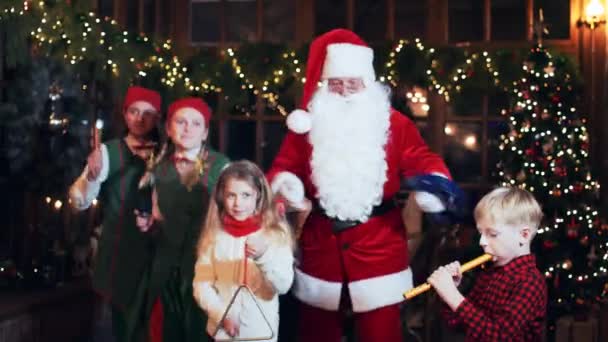 圣诞老人和孩子们一起跳舞 孩子们在房子里用圣诞树弹奏乐器 — 图库视频影像