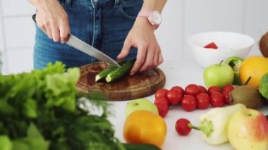 Kadın aşçı taze yeşil bir salatalığı tahta bir kesme tahtasına bıçak ile keser. Sebzeli masa ve salata yapmak için meyve..