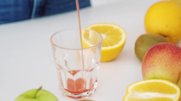 生のグレープフルーツジュースをグラスに注ぐ キッチンテーブルの上の果物 — ストック動画