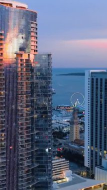 Günbatımında Miami 'de cam gibi modern binalar. Okyanusun arka planında akşam parlayan şehir manzarası. Pencerelerdeki yansımalar. Dikey.