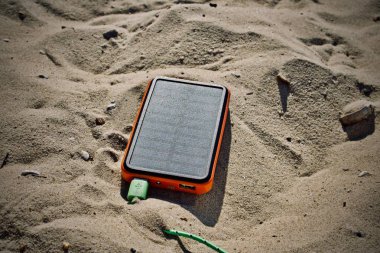 Plajda turuncu güneş enerjisi şarj cihazı. Yeşil kablo ile USB soket.