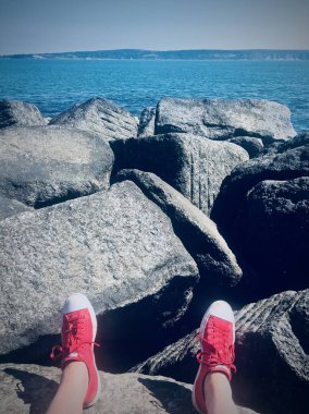 Kırmızı ayakkabılı adam. Okyanus manzaralı yaz konsepti. Suyun yakınında büyük taşlar.