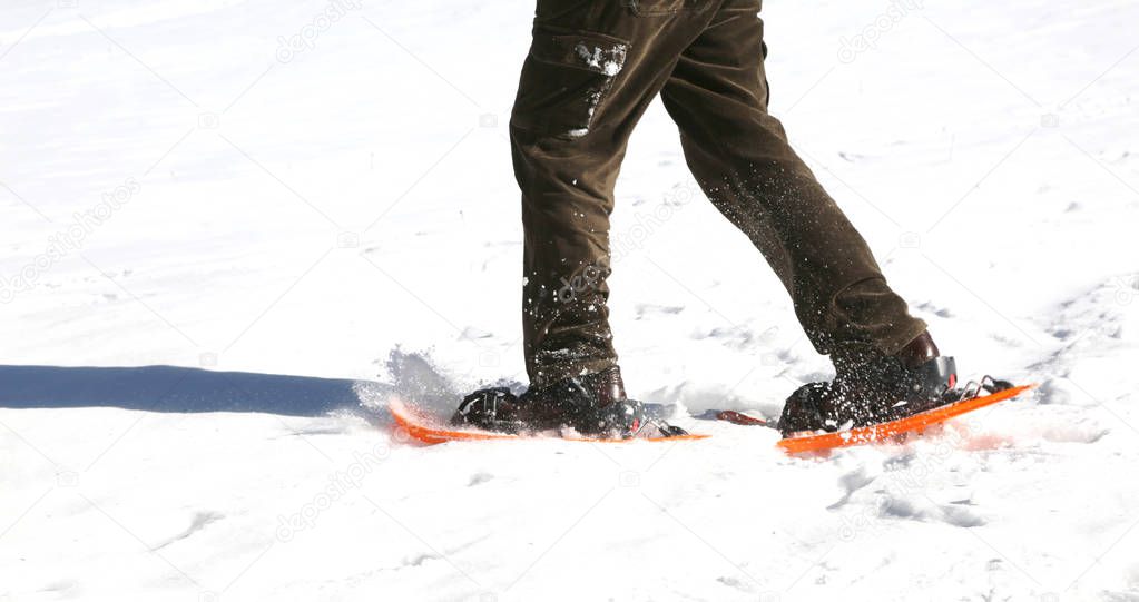 person walking on fresh snow fallen in winter using orange snowshoes