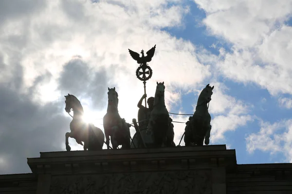 背光的勃兰登堡门在柏林德国与四匹马的剪影与多云的天空 — 图库照片