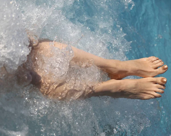 legs of a lady who relaxes in the hot tub of a swimming pool in a tourist village