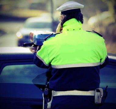 Polis arabası ve fosforlu bir üniformalı polis vintage etkisi ile acil arama sırasında cep telefonu kullanır