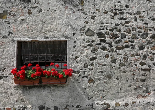 pots with geraniums with red flowers on the balcony of a stone house