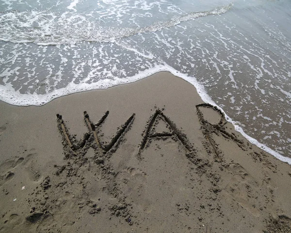 単語の戦争は水から消去している間はビーチの砂の上に書かれました — ストック写真