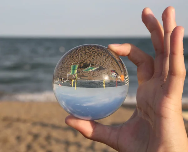 hand of a boy with a big sphere in glass on the beach by the sea