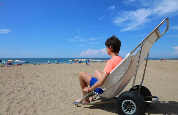 男孩乘坐特殊轮椅在沙滩上平稳地在夏天的海边移动 — 图库照片