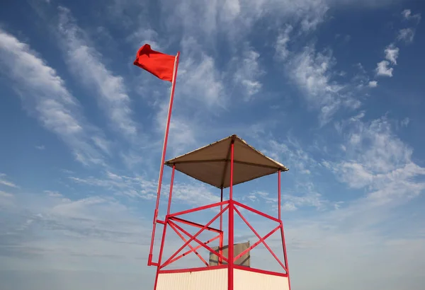風になびかせて大きな赤い旗が付いている浜のライフガードものみの塔 — ストック写真