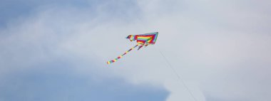Colorful kite flies in the clouds of the sky on a summer day clipart