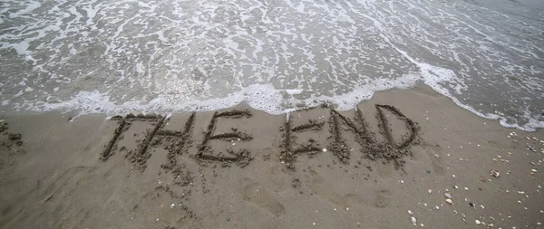 wide text THE END that is deleted by the sea wave on the sandy beach