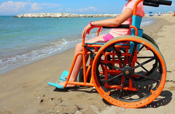 little girl on the wheelchair with special metal wheels to go on the beach by the sea