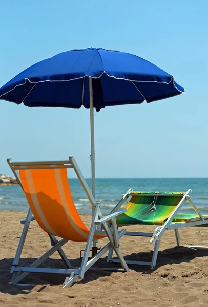 蓝色海滩伞和两个椅子在一个旅游村庄的海滩上 — 图库照片