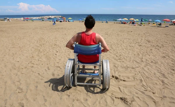young man on wheelchair with big special aluminum wheels on the beach of tourist village in summer
