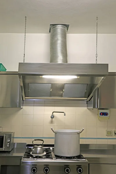 large hood of the industrial kitchen with a gigantic metal pot on the stove and a steel teapot