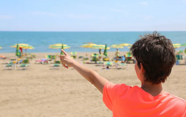 少年は オレンジ色の シャツとビーチから海を示しています — ストック写真