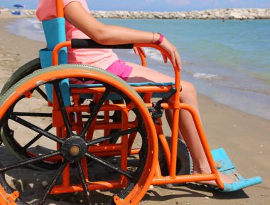 kumlu sahilde deniz kenarında taşımak için modifiye tekerlekli sandalyedeki küçük kız
