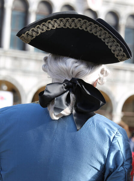 Masked person with big hat and wig during Venetian Carnival festival