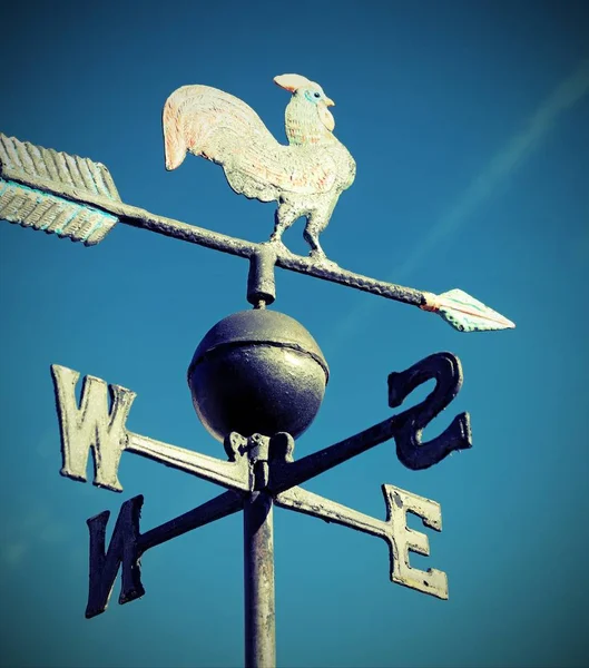 old wind vane with cock on top and cardinal points on the blue s