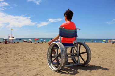 young boy on the special wheelchair on the sand of beach clipart