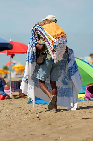 Vendedor de alfombras callejeras camina en la playa soleada —  Fotos de Stock