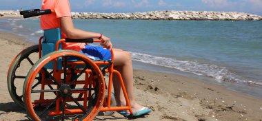 çocuk denize bakan bir tekerlekli sandalyede oturur