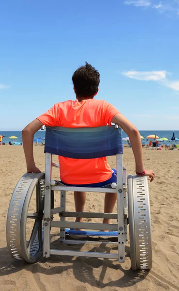 Menino em cadeira de rodas com rodas de alumínio grandes na praia perto do — Fotografia de Stock