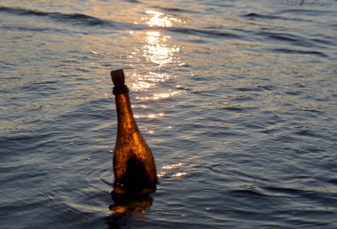 güneşte denizde yüzen bir mesaj içeren cam şişe