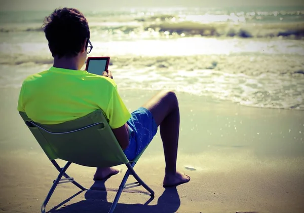 Chłopiec czyta ebook na krześle plażowym w lecie — Zdjęcie stockowe