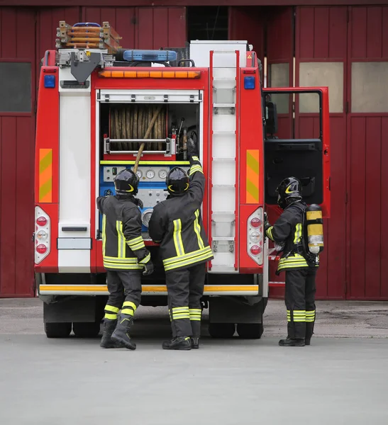 Три пожарных в действии и пожарная машина — стоковое фото