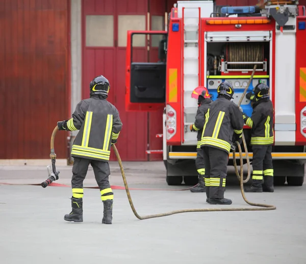 Three firefighters in action and the fire engine with hose — Stock Photo, Image