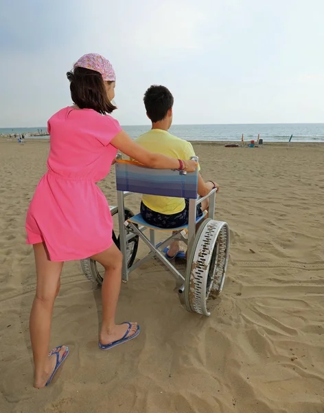 어린 소녀와 함께 해변에서 휠체어를 움직입니다. — 스톡 사진