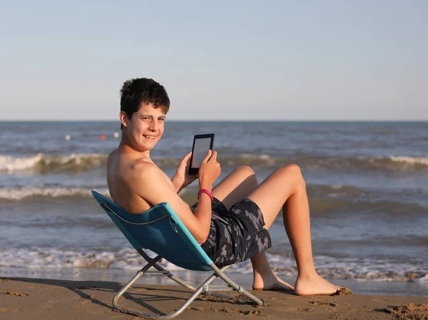 Pojke vid havet läser ebook på stranden — Stockfoto