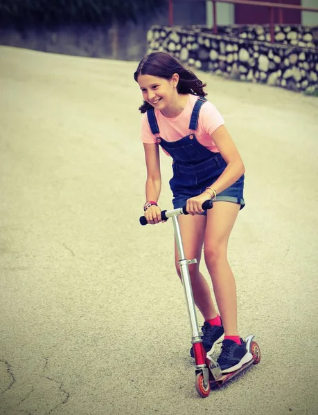 Snel klein meisje op scooter met tuinbroek jeans en oude gestemde e — Stockfoto
