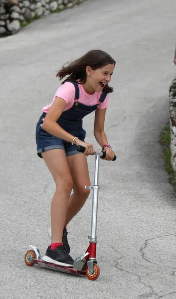 Menina corre em scooter com dungarees — Fotografia de Stock