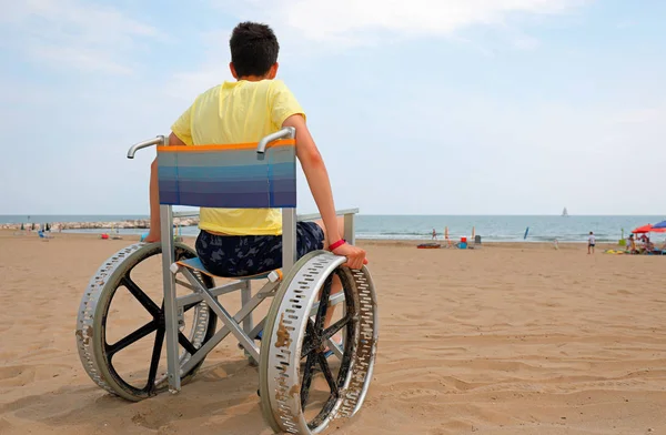 Niepełnosprawny chłopiec na wózku inwalidzkim na plaży — Zdjęcie stockowe