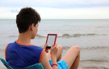 çocuk denize bakan bir dijital kitap okur