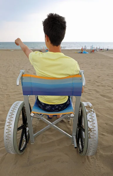 Niepełnosprawny chłopiec na wózku wskazuje na morze — Zdjęcie stockowe