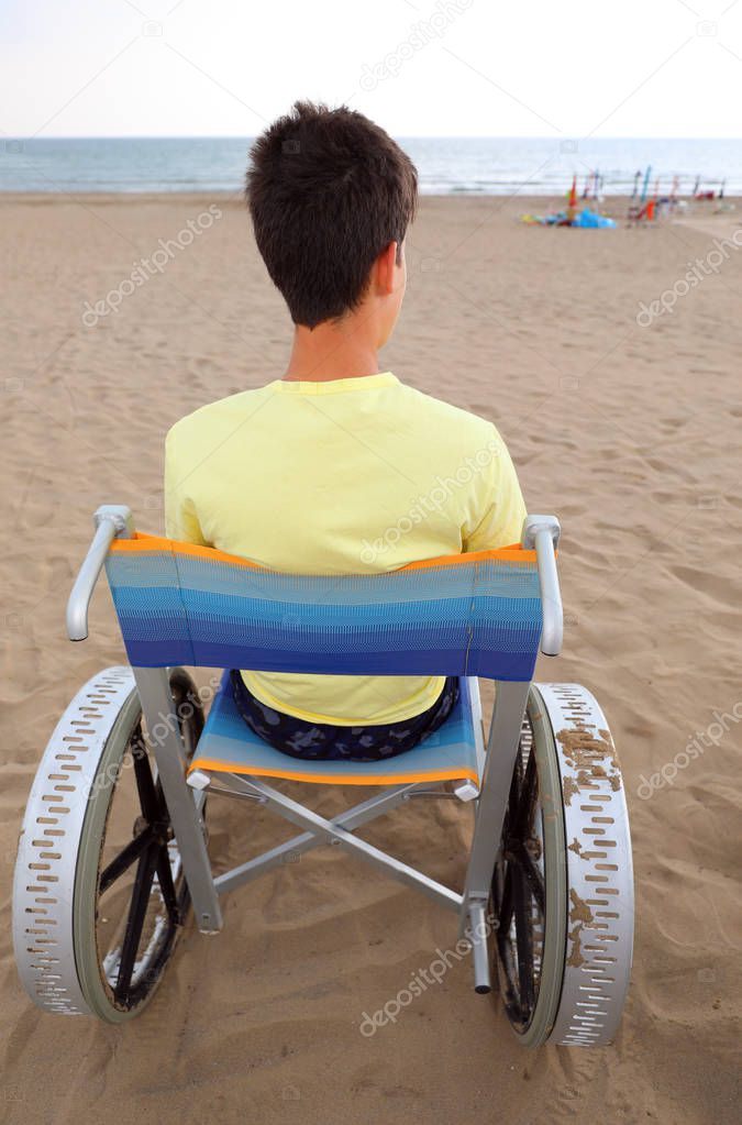 young boy on a special wheelchair in the beach in summer