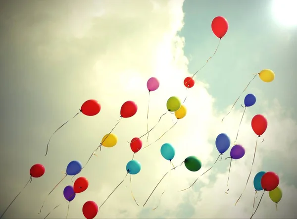 many colored balloons fly to the light on the blue sky