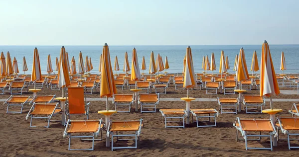 Closed umbrellas with deckchairs on the beach without people in — ストック写真