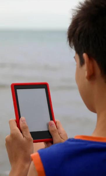 Młody chłopak czyta ebook na plaży w lecie — Zdjęcie stockowe