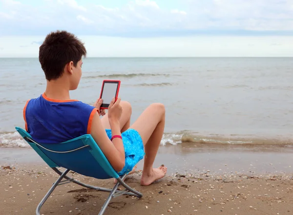 Молодой читатель читает электронную книгу на пляже — стоковое фото