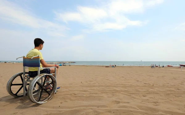 Menino em uma cadeira de rodas olha para o mar — Fotografia de Stock