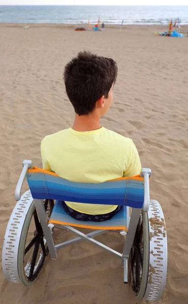 휠체어를 탄 어린 소년 이 모래 해변에서 바다를 바라본다 — 스톡 사진