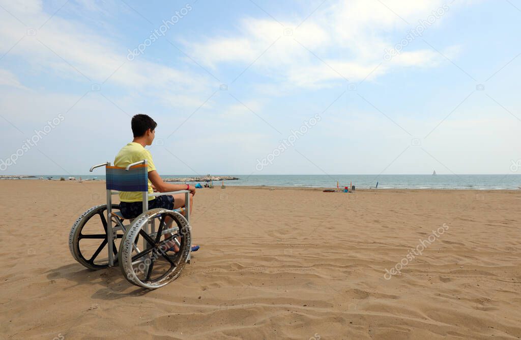 young boy on the wheelchair by the sea in summer