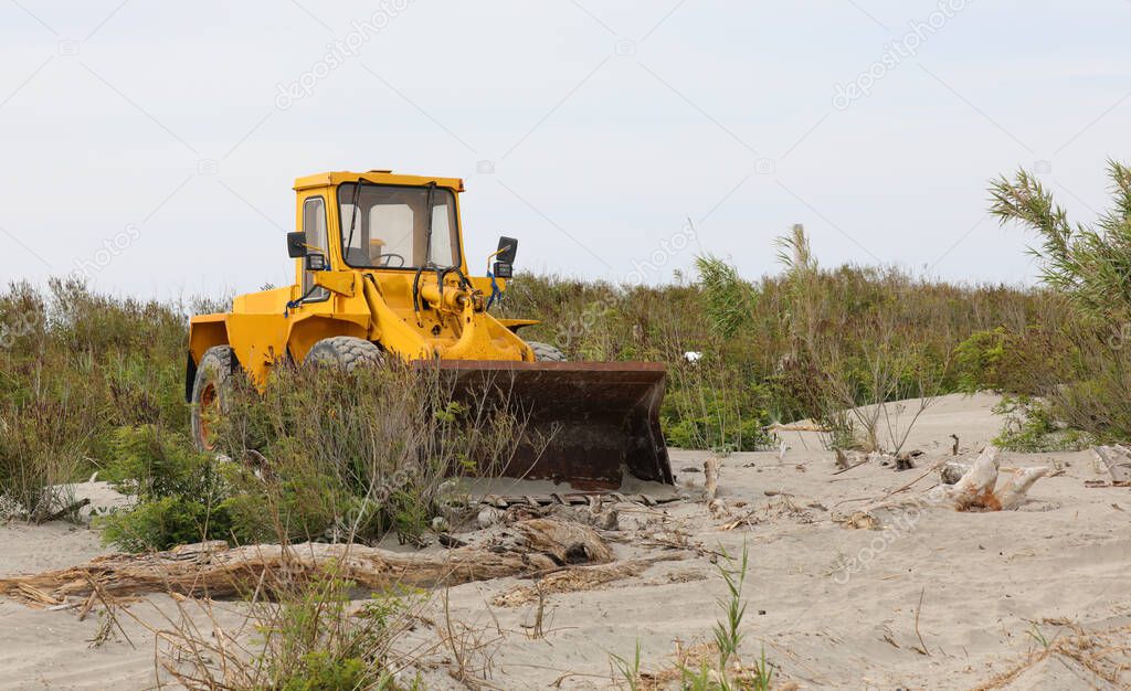 large yellow bulldozer on the sandy hills during the cleaning of the beach before the opening of the tourist season